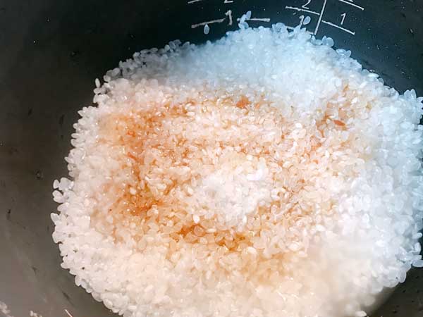 炊飯器に研いだ米と水とサンマ缶の汁を入れて混ぜ合わせる前の状態